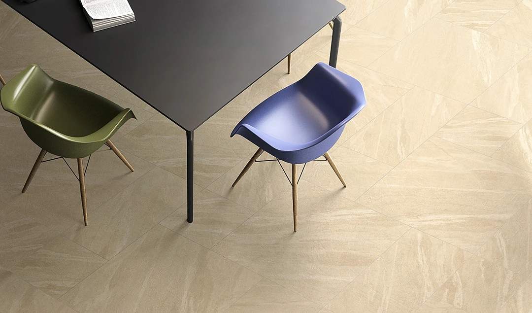 A black table with an open book on it is surrounded by a green chair and a blue chair, all set on a beige tiled floor that reflects sanitary elegance.